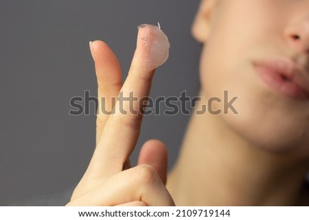 A young woman is applying petroleum jelly to her face. Concept of slugging. Royalty-Free Stock Photo #2109719144