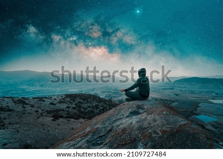 person sitting on the top of the mountain meditating or contemplating the starry night with Milky Way background
