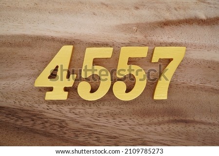 Wooden Arabic numerals 4557 painted in gold on a dark brown and white patterned plank background.