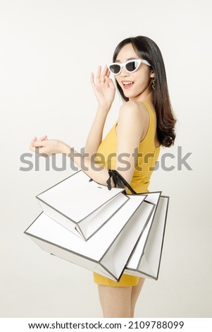 Portrait of Confident Asian woman in a sultry yellow dress wearing sunglasses and carrying a packages bag is having fun purchases after shopping isolated on white background. Royalty-Free Stock Photo #2109788099