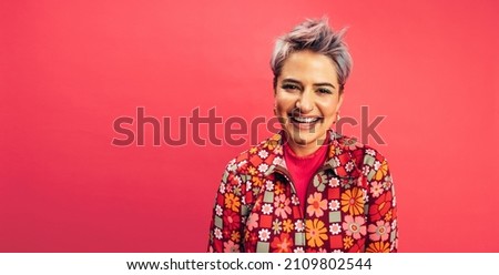 Hipster woman looking at the camera with a happy smile on her face. Cheerful young woman standing alone against a red background. Fashionable young woman with dyed hair feeling vibrant.