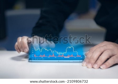 A young man in a coat is scrolling through the digital screen of his mobile phone with his hands. And use your hand to scroll the screen and see the stock chart that is being displayed.