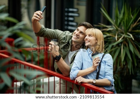Happy couple with takeaway coffee having fun while taking selfie in the city.