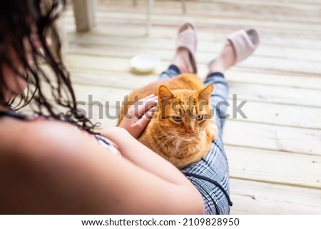 Young woman sitting on floor holding in arms lap cat lying down petting stroking feline orange ginger kitty outside at home house balcony porch patio