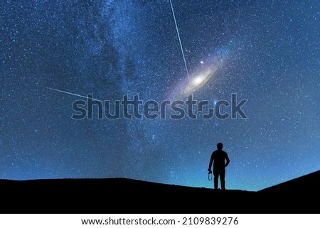 Silhouette of a person on the hill in starry night sky.  Bright andromeda galaxy and meteors behind him.