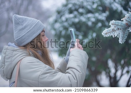 young woman takes pictures on the phone of winter pine branches, beautiful blonde with a phone in a winter park.