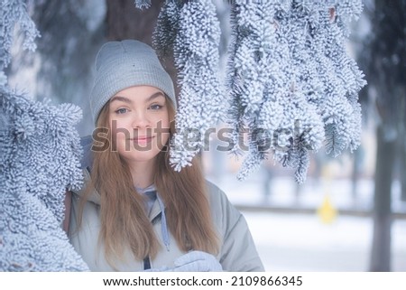 blonde in a gray hat in a snowy park, portrait of a woman against the background of frozen pine branches, Beautiful young woman in a winter forest