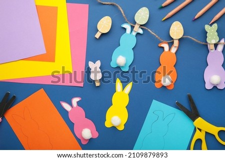 Easter bunnies handmade from colored paper, easy crafts for kids on a blue background. Top view.