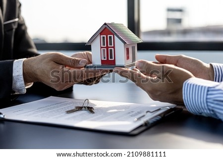 Two people holding a small model house, the home salesman handing over the house to the customer after signing the contract and inspecting the house. Real estate trading ideas.