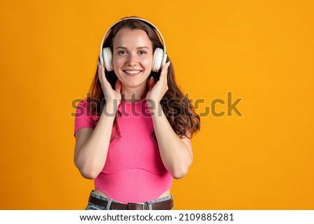 Music style. Portrait of young beautiful girl listening to music in headphones isolated over orange studio backgroundConcept of human emotions, facial expression, beauty. Copy space for ad