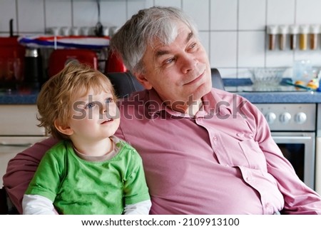 Little toddler boy and grandfather watching tv together. Happy family, grandchild and senior man, granddad at home, watch cartoons on television, indoors.