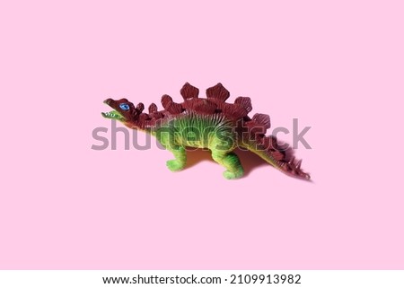 Green plastic toy stegosaurus isolated on a pastel pink background. Minimal kids dinosaur game playful concept poster.