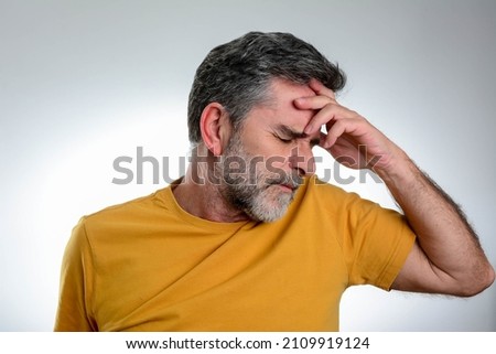 Mature Man having a headache isolated over grey background. Picture showing how much his head hurts, experiencing pain, looking miserable and exhausted.