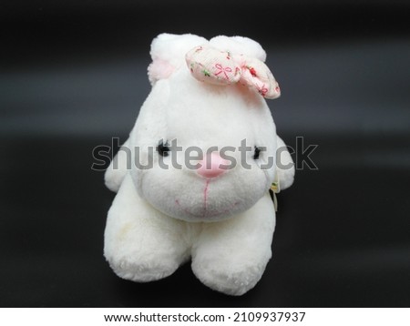 White cute rabbit doll toy sitting on black wood table. Dark background.
