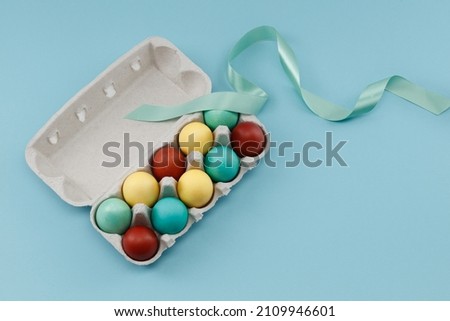 Easter colorful eggs in a dozen egg carton with ribbon on blue background  Royalty-Free Stock Photo #2109946601