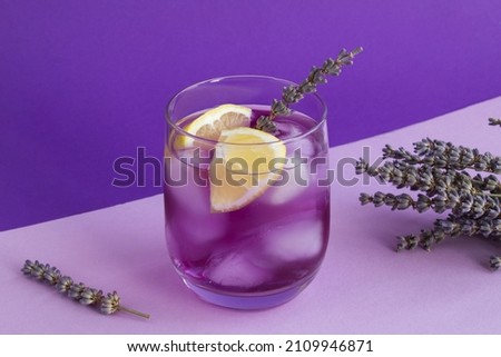 Lavender lemonade with ice and  lemon in the drinking glass on the purple background. Close-up. Royalty-Free Stock Photo #2109946871