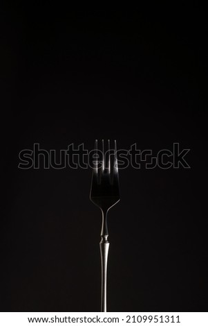 Stylish steel black fork on a dark background. Close-up. Monochrome. Vertical position. Copy space Royalty-Free Stock Photo #2109951311