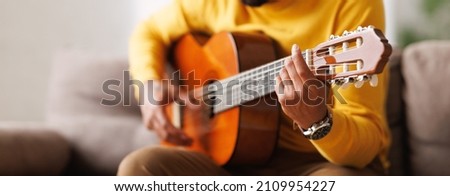 Panoramic banner with african american man playing on acoustic guitar, sitting on sofa at home. Guitarist holding musical instrument, website header banner for music shop. Musical education concept Royalty-Free Stock Photo #2109954227