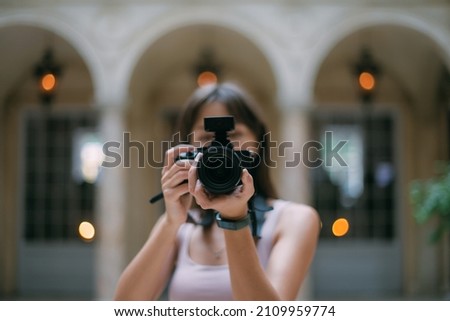 Portrait of a tourist girl with a camera in her hands in the hall of the museum. Young beautiful woman takes pictures on excursions while traveling on vacation. Royalty-Free Stock Photo #2109959774