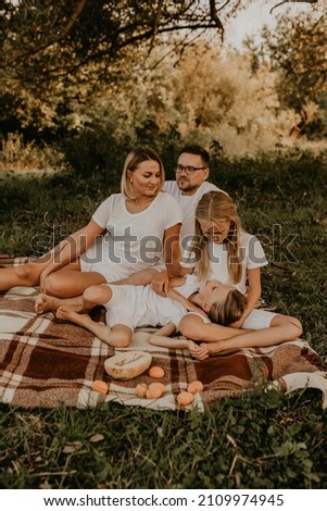 cheerful happy family dad mom daughters sit picnic plaid blanket bedspread. have fun playing at summer outdoors together. father mother sisters parents hugging kissing. Family resting under big tree