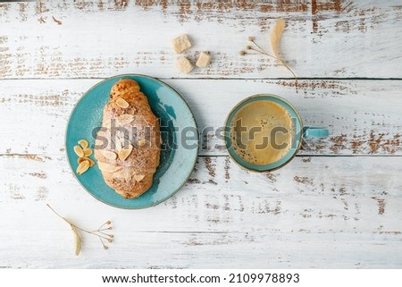 Fresh baked almond nuts breakfast croissant on vintage turquoise plate and hot coffee cup on rustic wooden background. Top view pastry good morning card with copy space