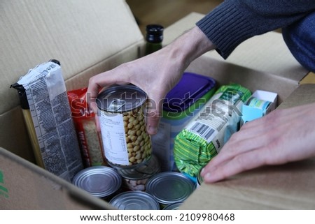 Donation cardboard box with various food (pasta, rice, oil, tuna, canned goods...) and a man's hands adding a chickpeas can.. Royalty-Free Stock Photo #2109980468