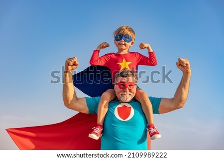 Superhero senior man and child playing outdoor. Super hero grandfather and boy having fun together against blue summer sky background. Family holiday concept. Happy Father's day Royalty-Free Stock Photo #2109989222