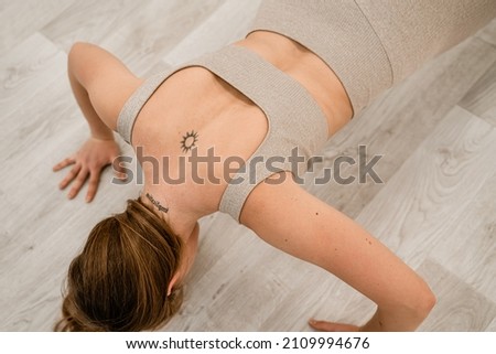 Top view of a muscular woman during push-ups. She is wearing a beige top and leggings, with a round tattoo between her shoulder blades. The concept of a healthy lifestyle.