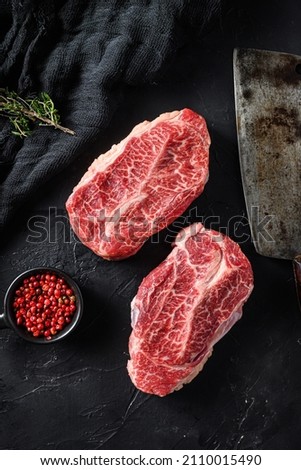 Raw  top blade flat Iron beef cut organic meat ner butcher meat clever knife for bbw or gtrill  over black stone background top view vertical Royalty-Free Stock Photo #2110015490