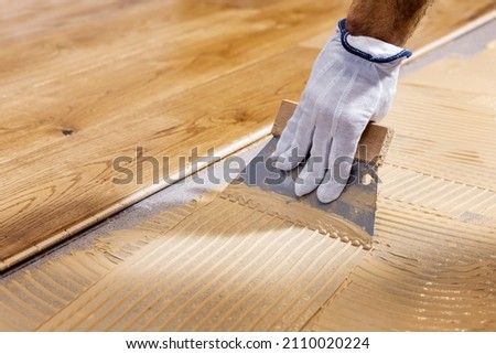 worker apply adhesive for 3 layer parquet flooring Royalty-Free Stock Photo #2110020224