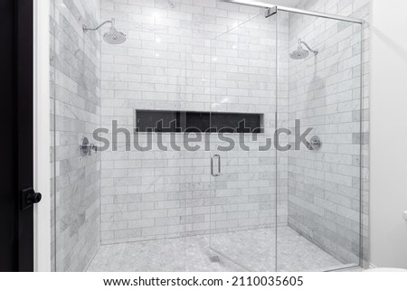 A large, luxury double shower with marble subway tile walls, marble hexagon floor, and black hexagon tiled shelf. Royalty-Free Stock Photo #2110035605