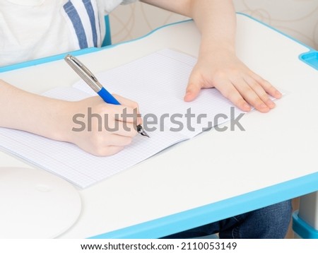A boy writing with a pen in a copybook. Hands close up. Focus on a pen. Royalty-Free Stock Photo #2110053149