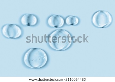 Cosmetic hydrating product or ingredient concept. Blue drops of transparent liquid on a light background. Drops gel or oil close up. Abstract backdrop. Royalty-Free Stock Photo #2110064483