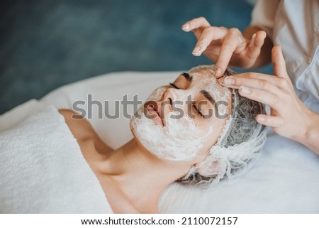 Woman face getting facial care with cream by beautician hands at spa salon. Close-up portrait. Royalty-Free Stock Photo #2110072157