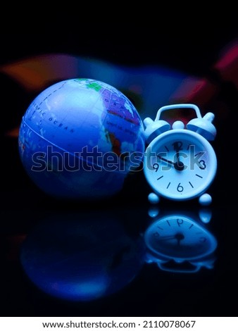 Earth globe and white clock with colorful reflection on a black background.
