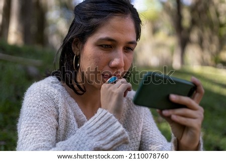 Young Latin American woman (29) sitting on the grass, looking at her cell phone. Communication concept.