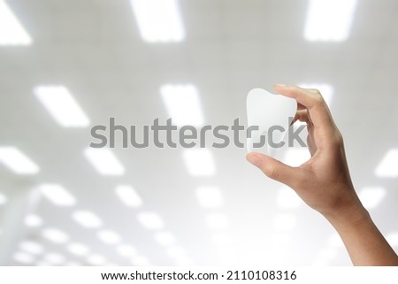 Hands holding tooth shape at blurred background.