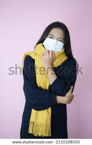 Young girl wear mask and sweater on pinkbackground.