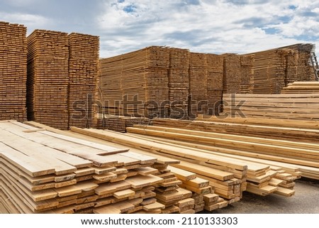Industrial production of finished lumber products stacked in stacks on the warehouse territory. On an open background of blue sky with clouds. Royalty-Free Stock Photo #2110133303