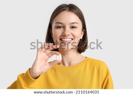 Young woman with chewing gum on light background