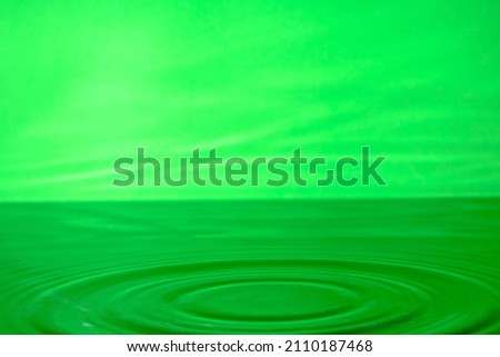 Bright green background with diverging circles from dropped drop on surface water