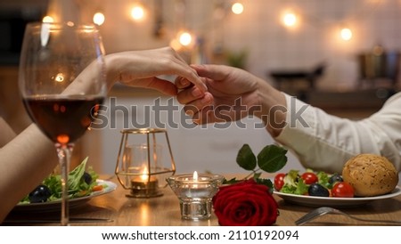 closeup with cropped shot of lovers holding hands over romantic valentine’s day dinner table with wine and red rose. the man gently touches the woman’s fingers. Royalty-Free Stock Photo #2110192094