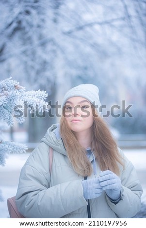 Beautiful young woman in the winter forest, portrait of a woman against the background of frozen pine branches in the park, blonde in a gray hat in a snowy park