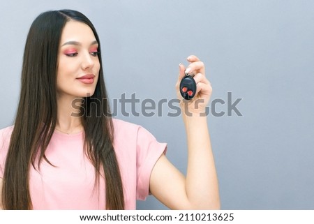 beautiful smiling young woman with car keys and a car in her hand. The concept of learning in a driving school and buying a new car. on a gray background