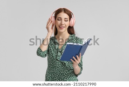 Young woman with headphones and book on grey background