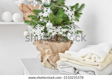 Beautiful Christmas tree in pot decorated with snowflakes, balls and warm clothes on table in room