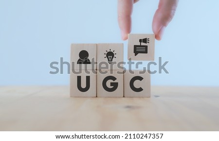 User-generated content concept.(UGC) Online marketing concept. Customer create content on social media . Close up hand put  wooden cube with "UGC"icon and abbreviation  on white background,copy space. Royalty-Free Stock Photo #2110247357