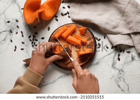 Woman cutting fresh pumpkin on white marble background