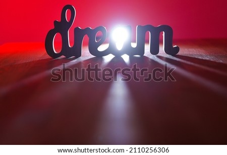 Dream concept. Wood letters spelling the word dream with dramatic lights and shadows. Red background.