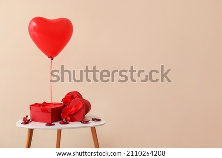 Table with gifts for Valentine's Day and balloon on color background